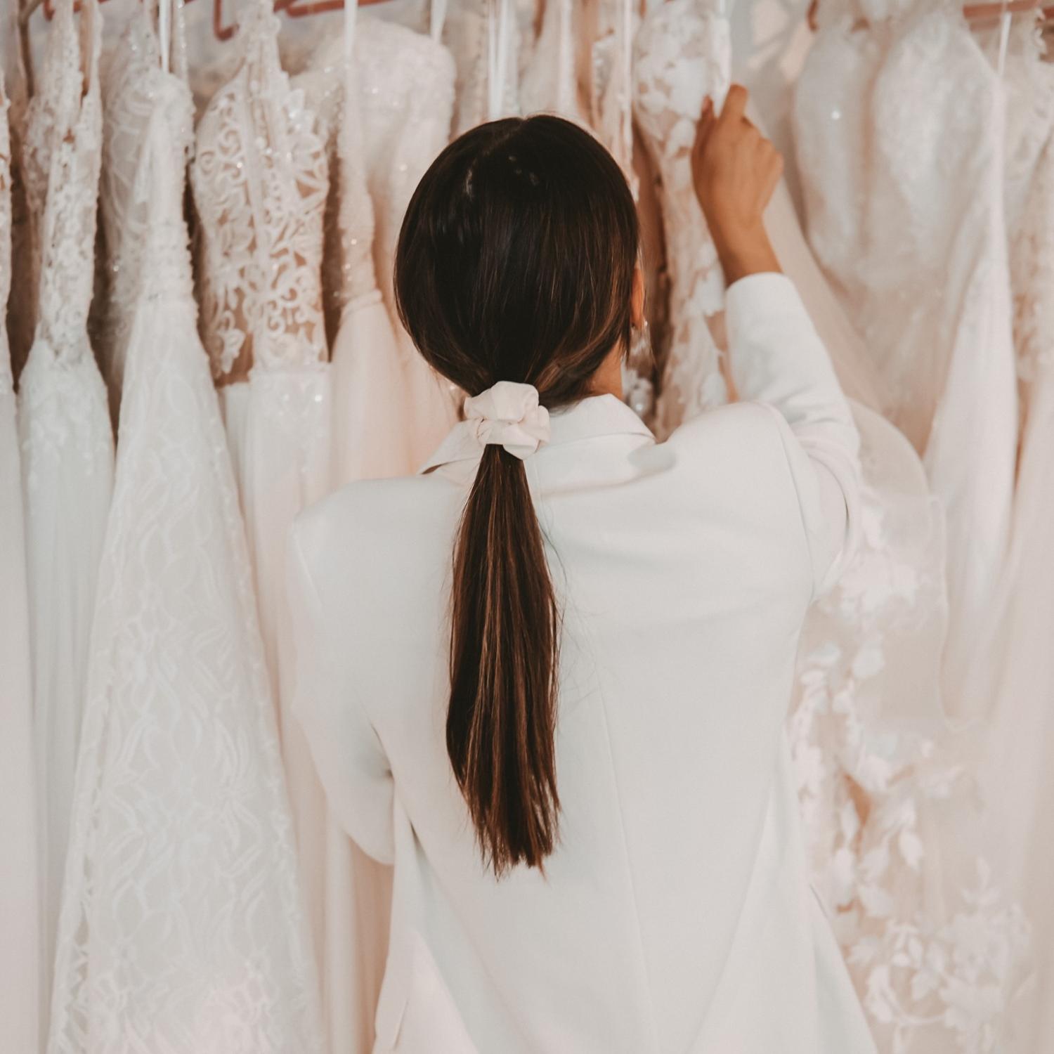 Rückansicht einer Stylistin vor Brautkleidern auf der Suche nach dem perfekten Kleid